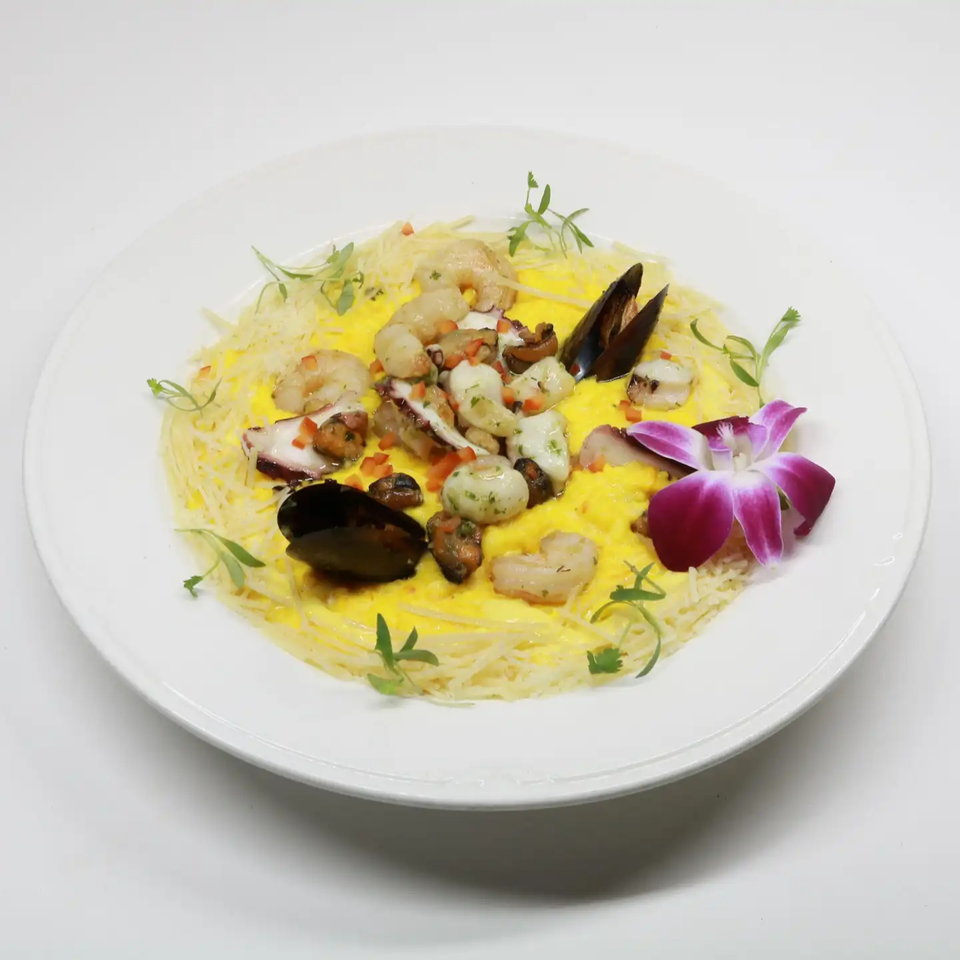 Peruvian seafood pasta with mussels, shrimp, octopus, and a purple orchid garnish on a white plate.