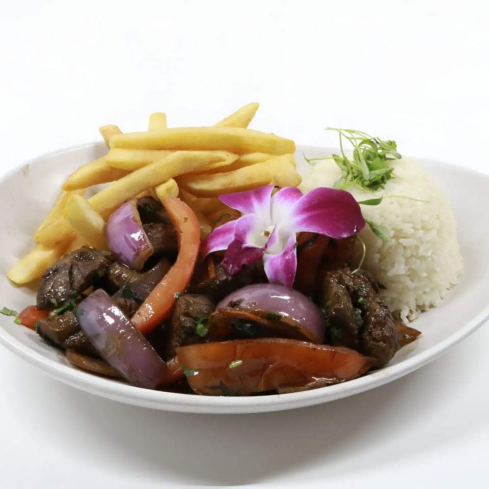 Peruvian Lomo Saltado with beef, onions, tomatoes, french fries, rice, and an orchid garnish.