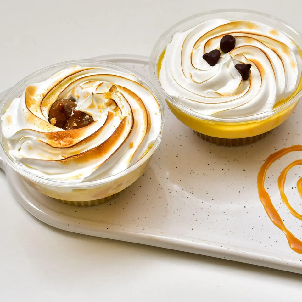 Two Peruvian desserts with toasted meringue topping, one with chocolate chips, on a white tray.
