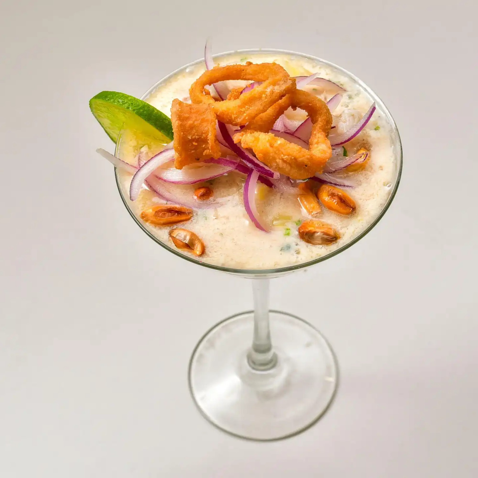 Peruvian leche de tigre cocktail with fried calamari, red onions, and corn in a martini glass.