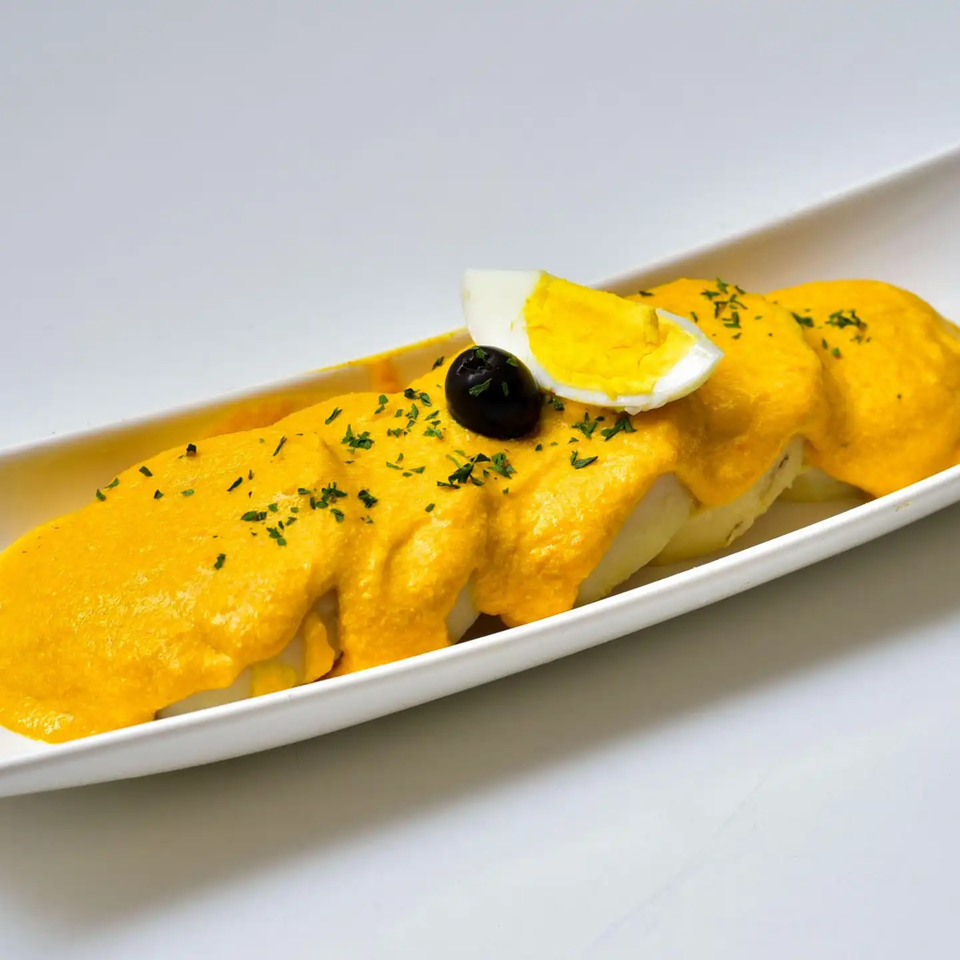 Peruvian Papa a la Huancaína with yellow sauce, parsley, a black olive, and hard-boiled egg.