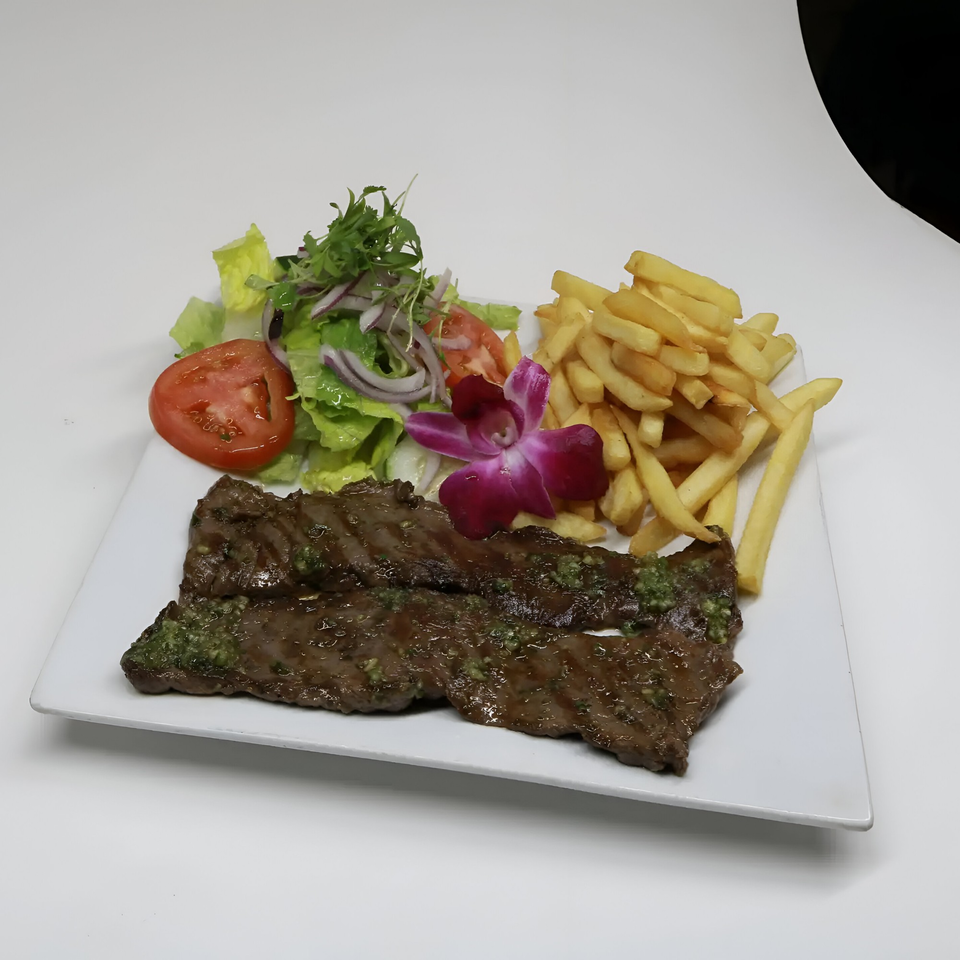 Peruvian grilled steak with green sauce, french fries, and a fresh salad with a purple orchid.
