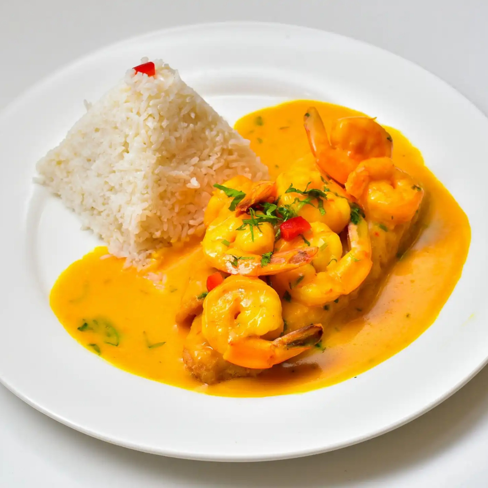 Peruvian Fusion Cuisine's shrimp in a vibrant yellow sauce with white rice, garnished with herbs and red pepper.