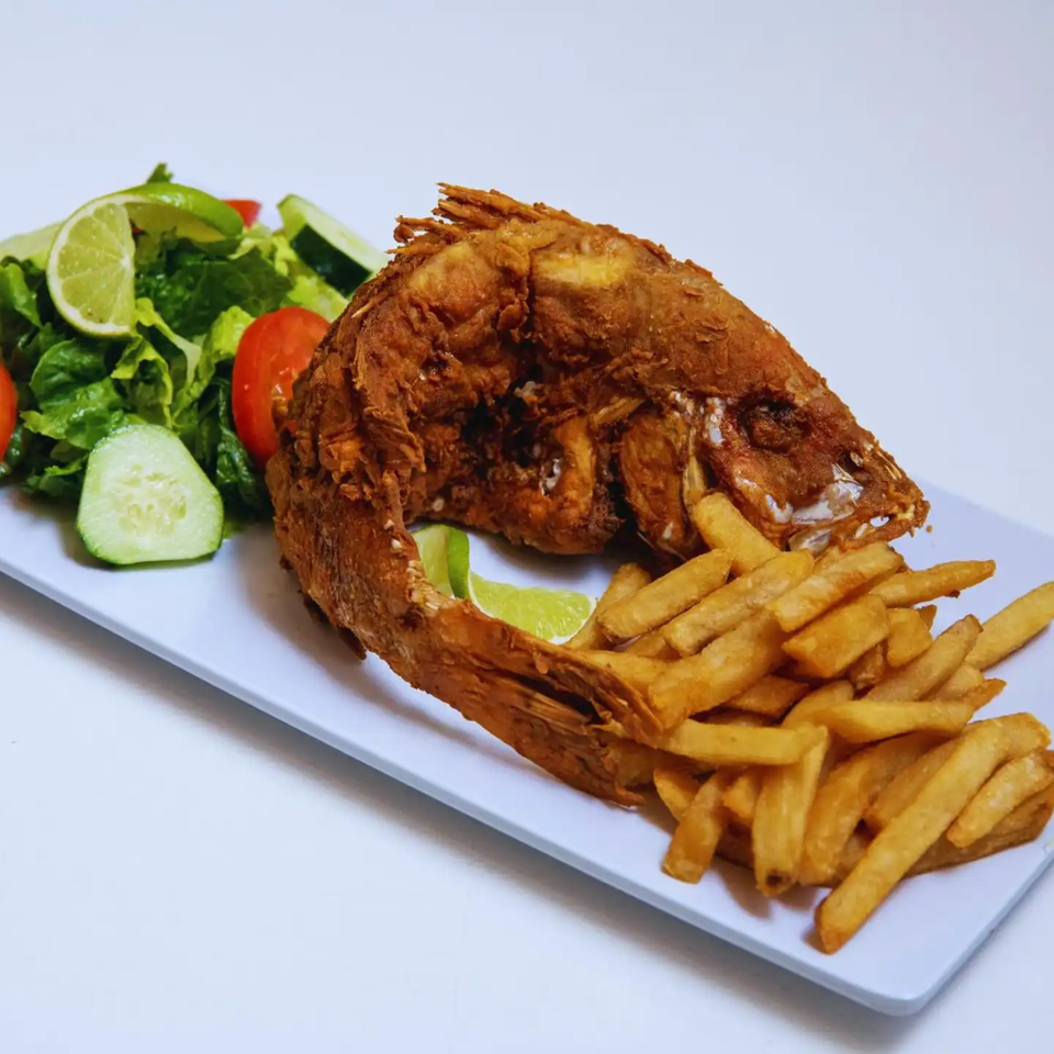 Whole fried Peruvian fish with french fries, a side salad, and lime wedges on a white plate.